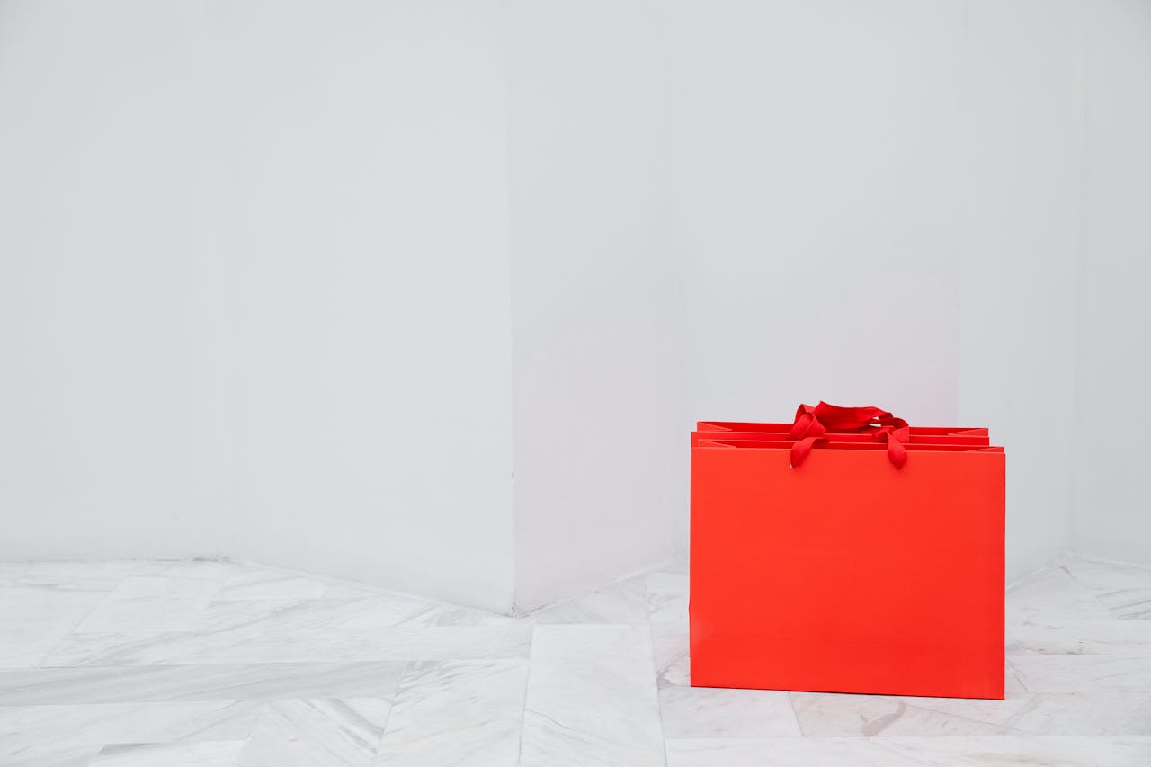 Red shopping bag on a marble floor against a white background, showcasing a minimalist style.